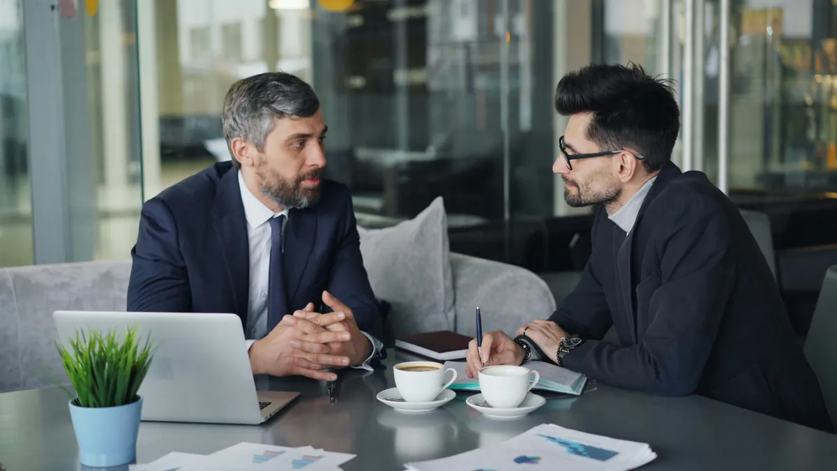 Due professionisti a un tavolo con laptop e appunti durante un incontro di lavoro