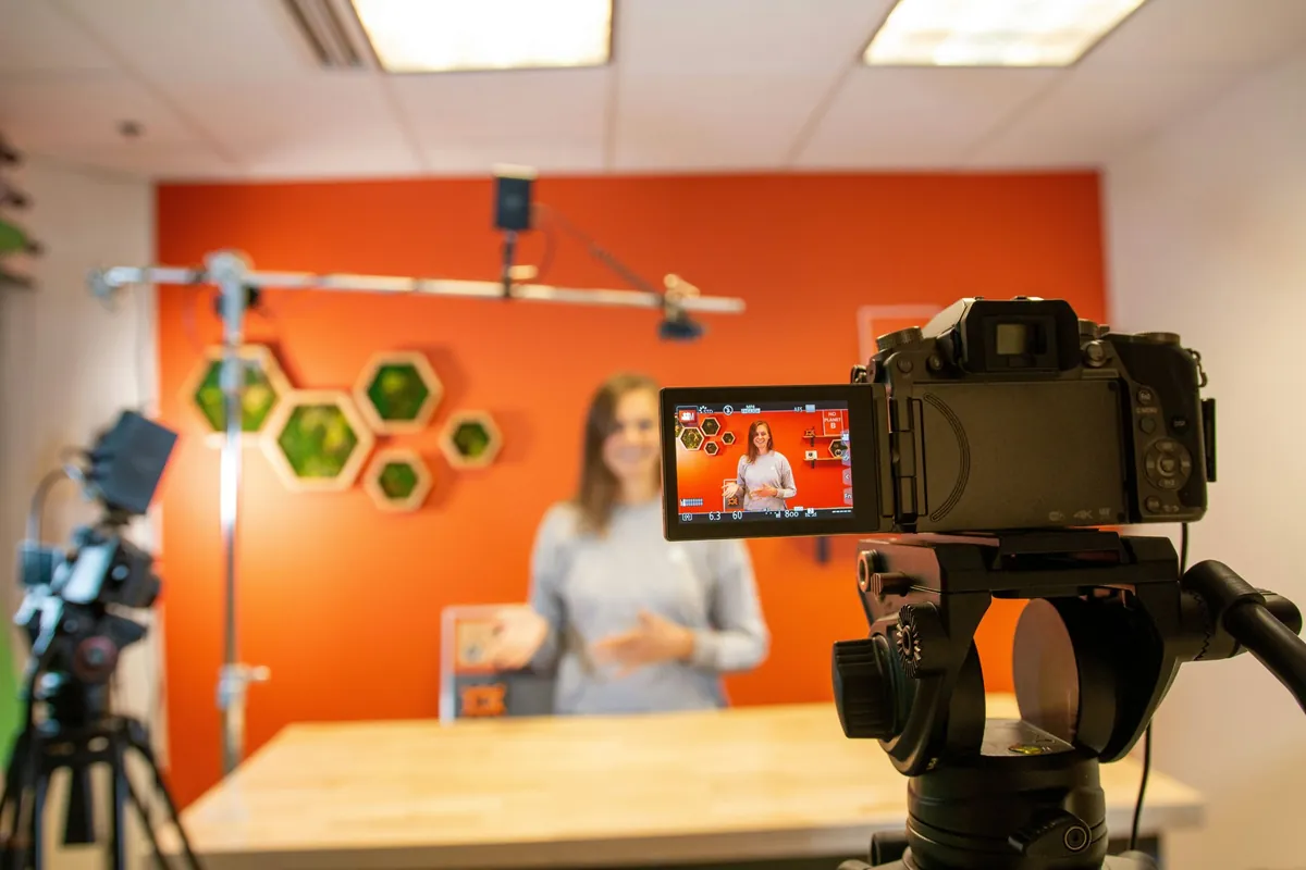 Fotocamera su treppiede che riprende una ragazza in uno studio con la parete arancione
