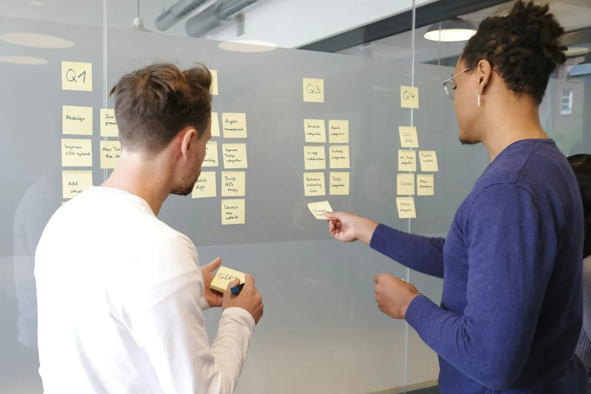 Due persone davanti a una parete di vetro organizzano post-it divisi per trimestre