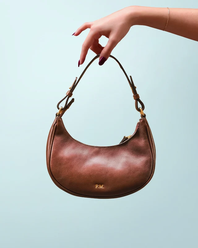 Borsa color cuoio sorretta da una mano su sfondo azzurro