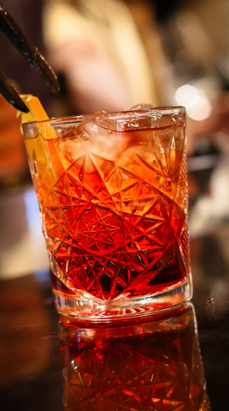 Cocktail ambrato con ghiaccio e scorza d’arancia in un bicchiere sfaccettato
